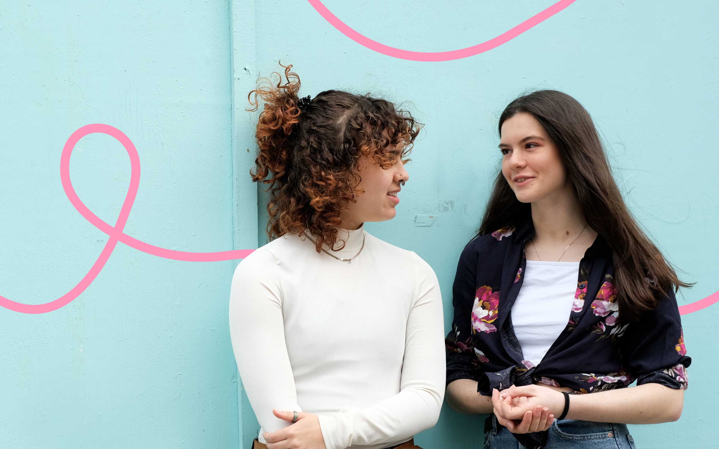 Two young female people standing against blue wall